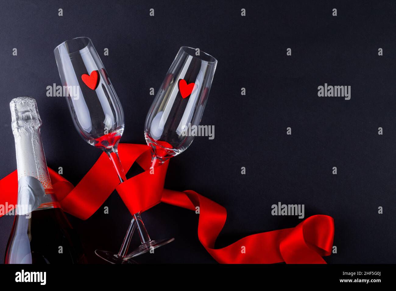 Formes de coeur dans des flûtes vides enveloppées d'un ruban rouge et d'une bouteille de champagne Banque D'Images