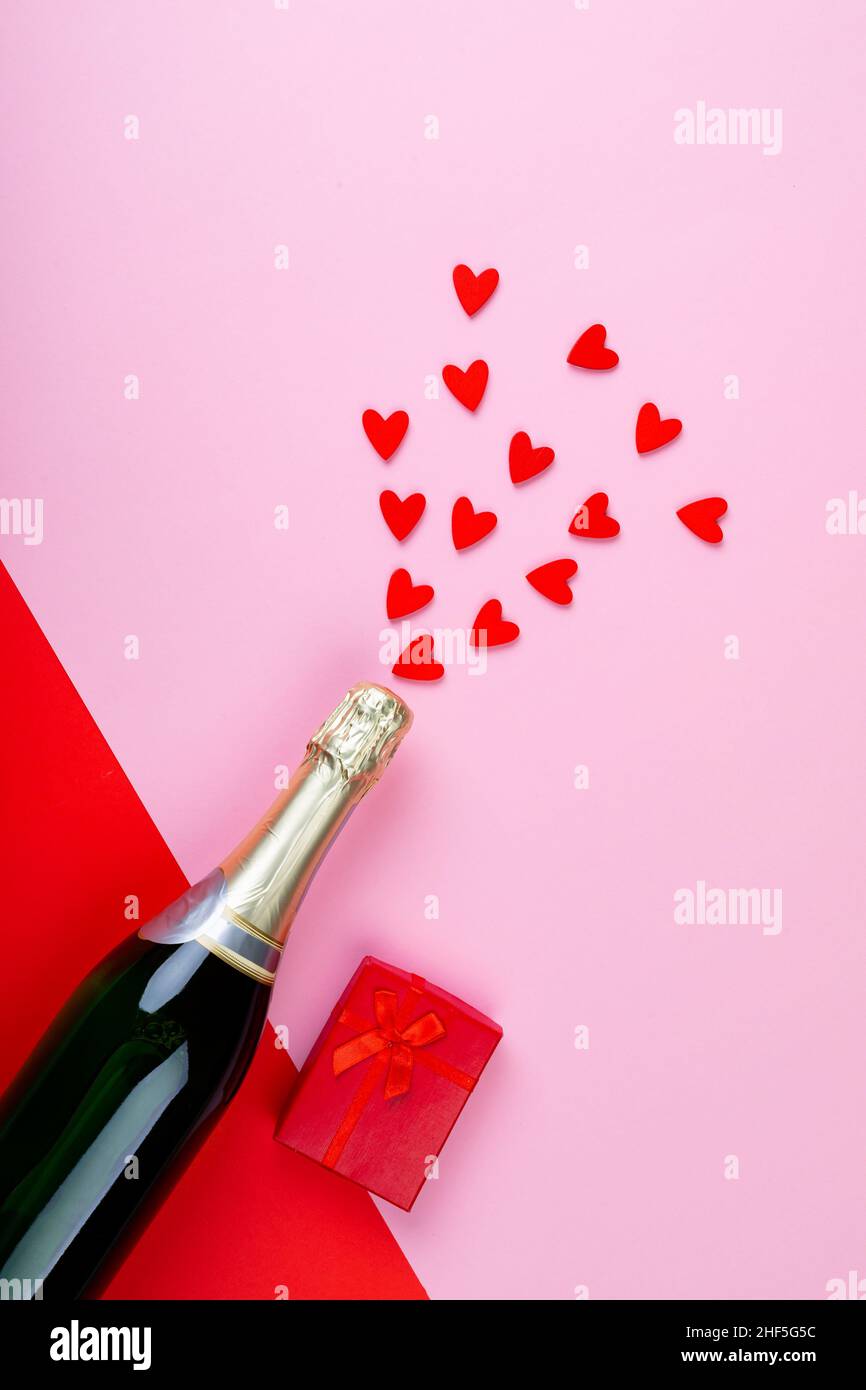 Bouteille de champagne éclaboussant les formes de coeur rouge par boîte-cadeau sur fond rose Banque D'Images