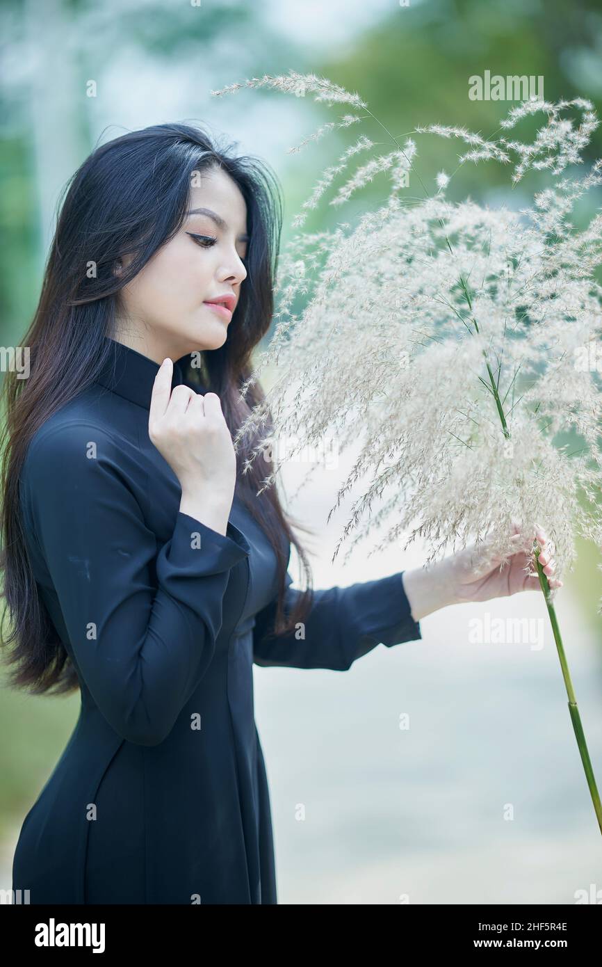 Ho Chi Minh ville, Vietnam: Belle fille vietnamienne en noir ao dai, posant pour une photo avec des mauvaises herbes Banque D'Images