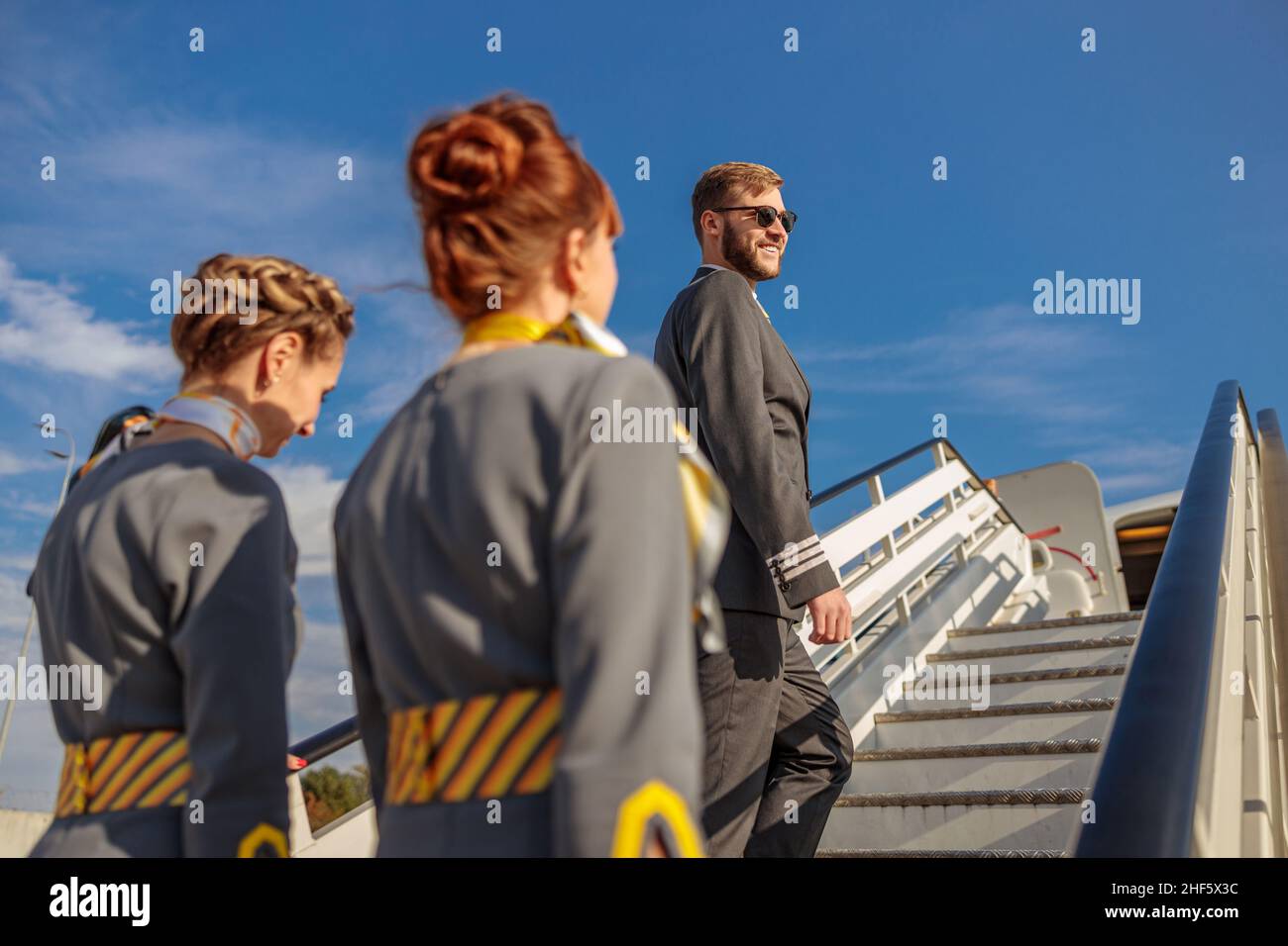 Homme souriant pilote et deux femmes de bord grimpant avion monter des escaliers sous le ciel bleu Banque D'Images