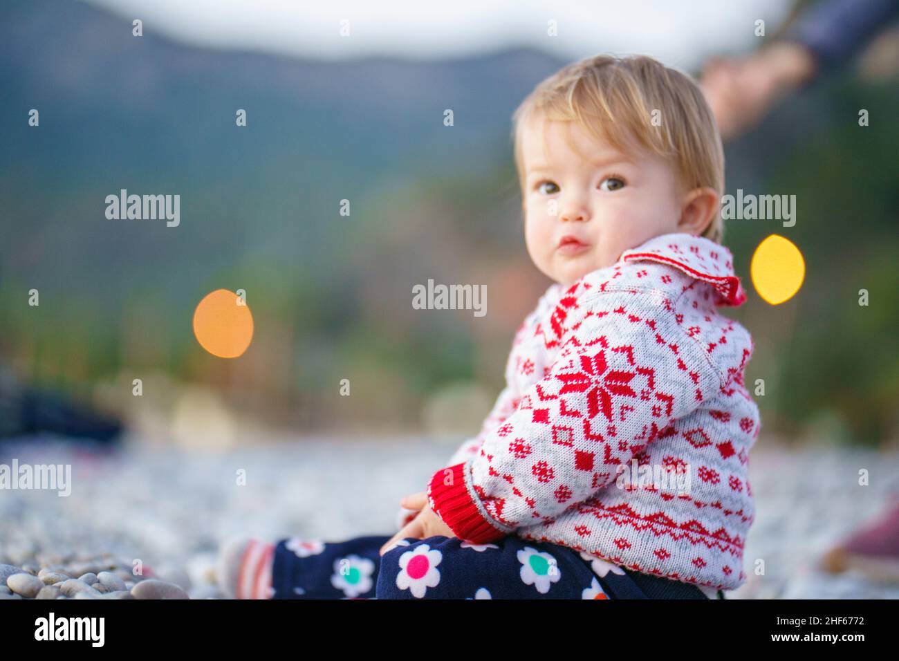 L'enfant est assis sur une plage en pierre.Un bébé mignon dans un magnifique chandail sur le rivage de la mer d'hiver.Beau enfant dans la nature. Banque D'Images