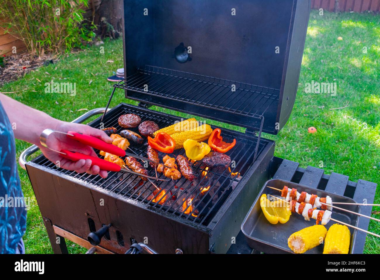 Les Britanniques profitent d'un week-end de vacances en banque dans le soleil de la vague de chaleur dans un jardin à l'arrière.Viande grillée à la flamme, hamburgers juteux, maïs sucré grillé au charbon et Banque D'Images
