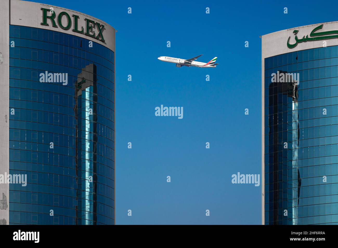 Avion blanc volant entre deux grands bâtiments à Dubaï, sous un ciel bleu clair Banque D'Images