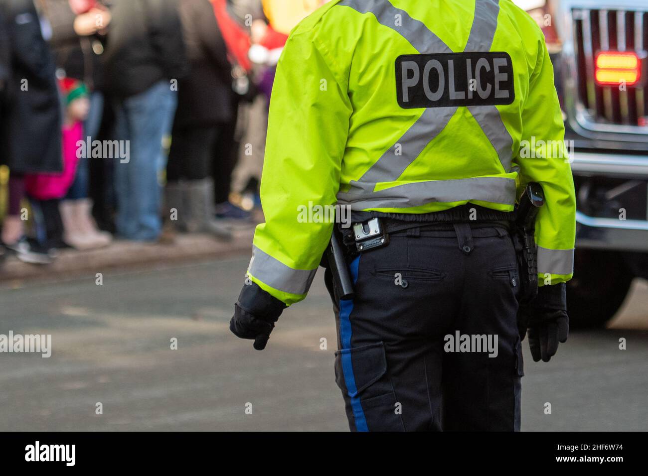 Policier, portant des vêtements fluorescents, debout dans une rue bondée.L'officier porte un gilet à l'épreuve des balles avec le mot police sur son dos Banque D'Images