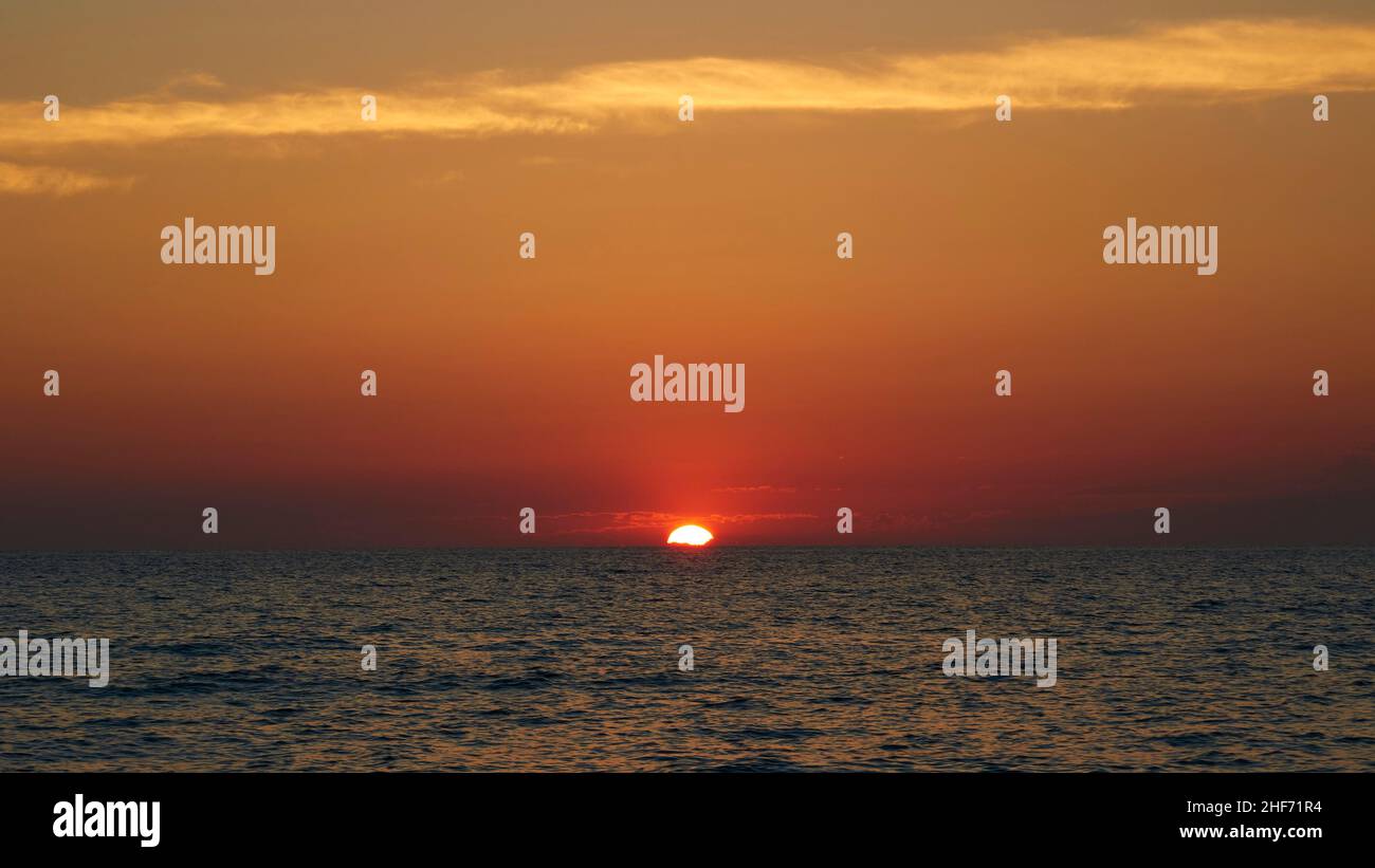 Grèce, Iles grecques, Iles Ioniennes, Corfou, côte ouest,Agios Gordios, prise de vue en soirée, coucher de soleil, le fils se couche dans la mer, mer légèrement déplacée, ciel orange-rouge, nuages au sommet de la photo Banque D'Images