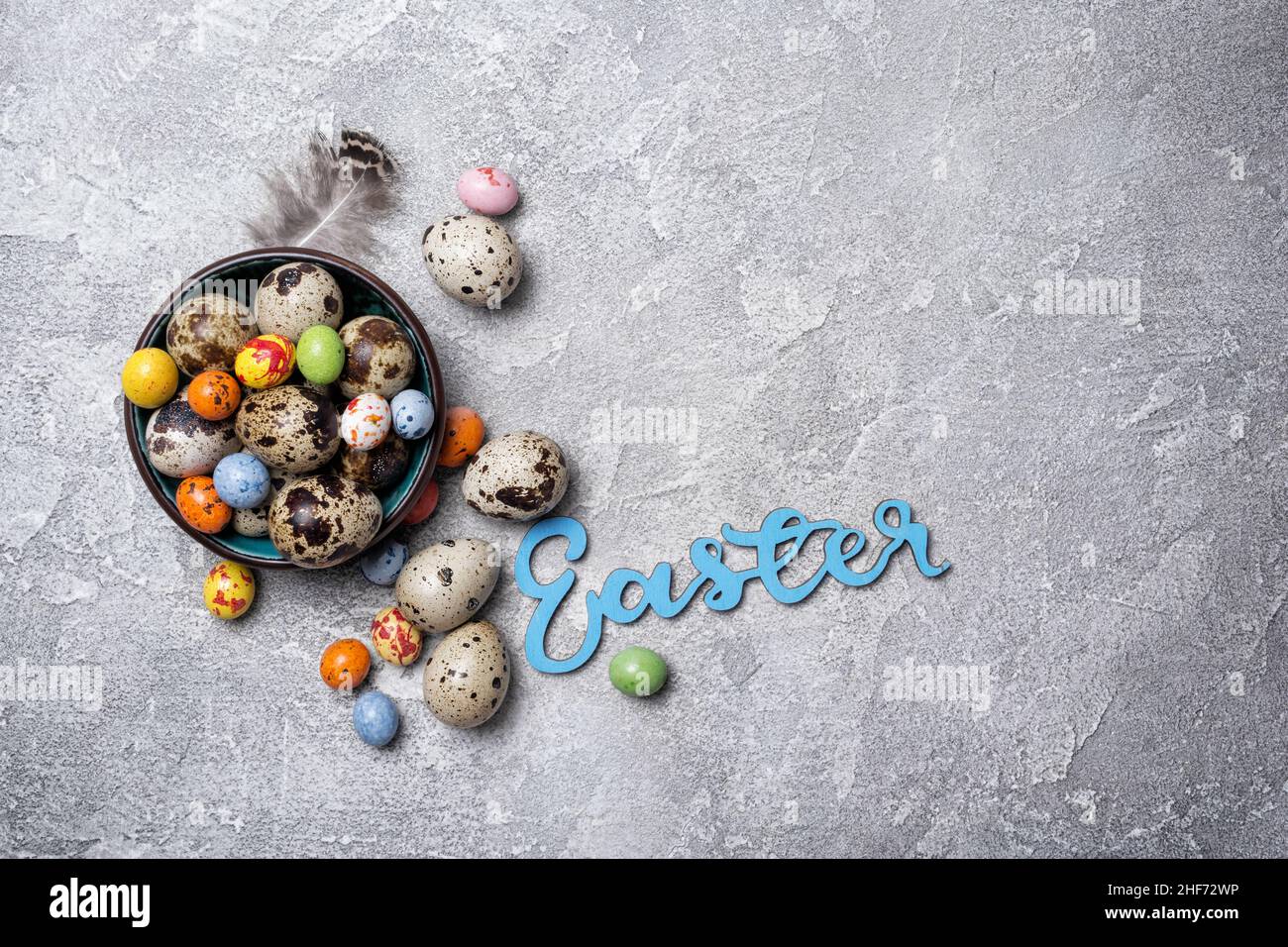 Vue de dessus de petits œufs de caille et de bonbons colorés dans un bol pour Pâques sur fond de béton gris Banque D'Images