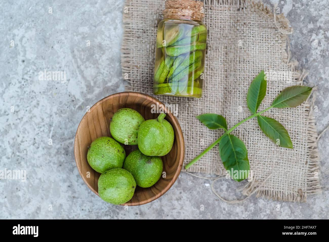 Noix vertes non mûres lisses et teinture de noix dans un pot transparent avec couvercle en liège sur une table ancienne.Feuilles sur la branche de l'écrou.Récupérer le ingre Banque D'Images