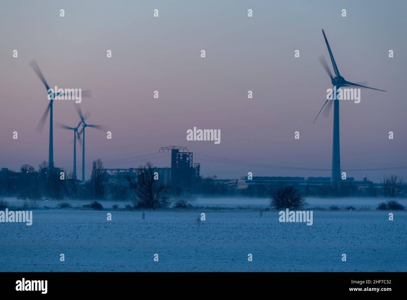 Les éoliennes tournent dans la zone industrielle de Rothensee, à Magdebourg, tandis que le soleil couchant décolore le ciel. Banque D'Images