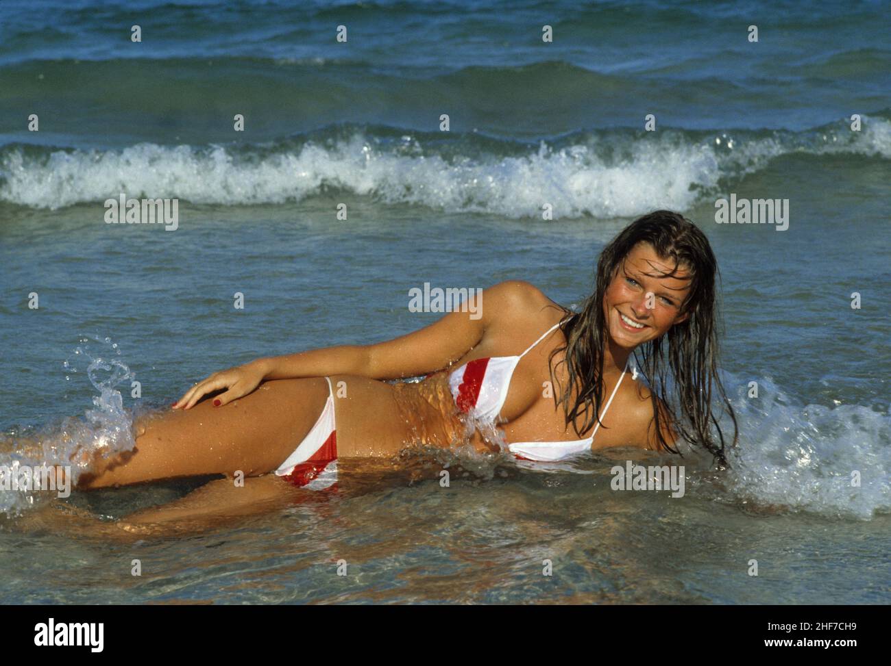 belle cheveux blond jeune femme en mer regarder devant caméra bleu eau de mer fond naturel visage souriant face avant caméra Banque D'Images
