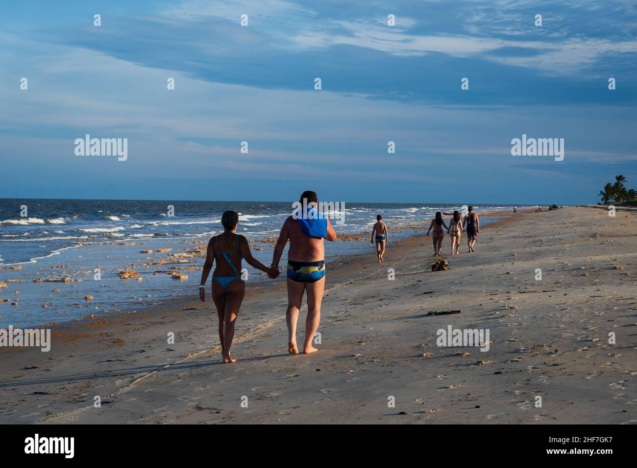 Vue arrière des amateurs de plage marchant sur le sable tenant les mains à la plage de Guaratiba, Prado, Bahia, Brésil pendant le coucher du soleil. Banque D'Images