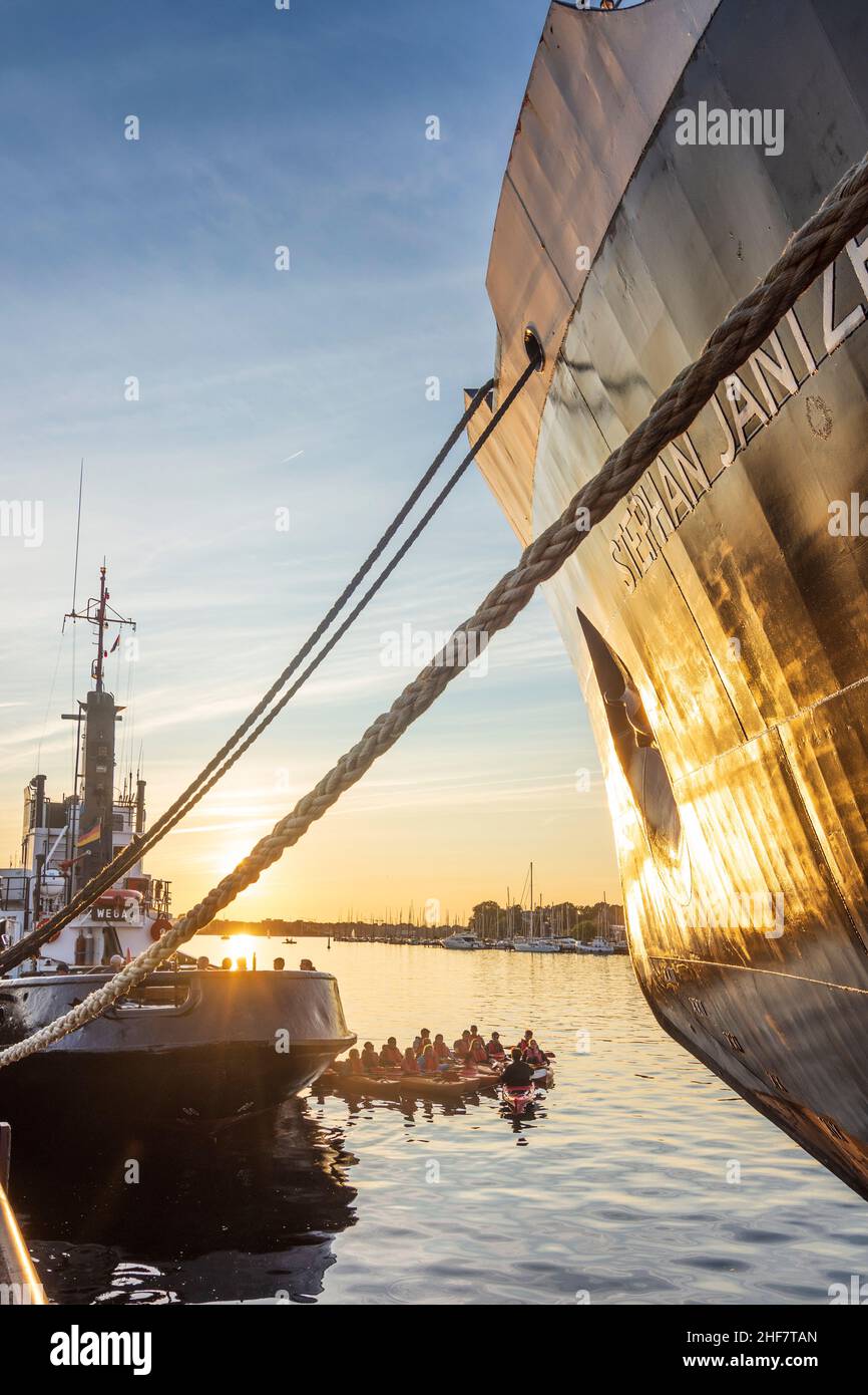 Rostock, Stadthafen (port de la ville), brise-glace de navire de musée 'Stephan Jantzen' (à droite), groupe de pagayeurs entre grands navires, coucher de soleil à Ostsee (mer Baltique), Mecklembourg-Poméranie-Occidentale, Allemagne Banque D'Images