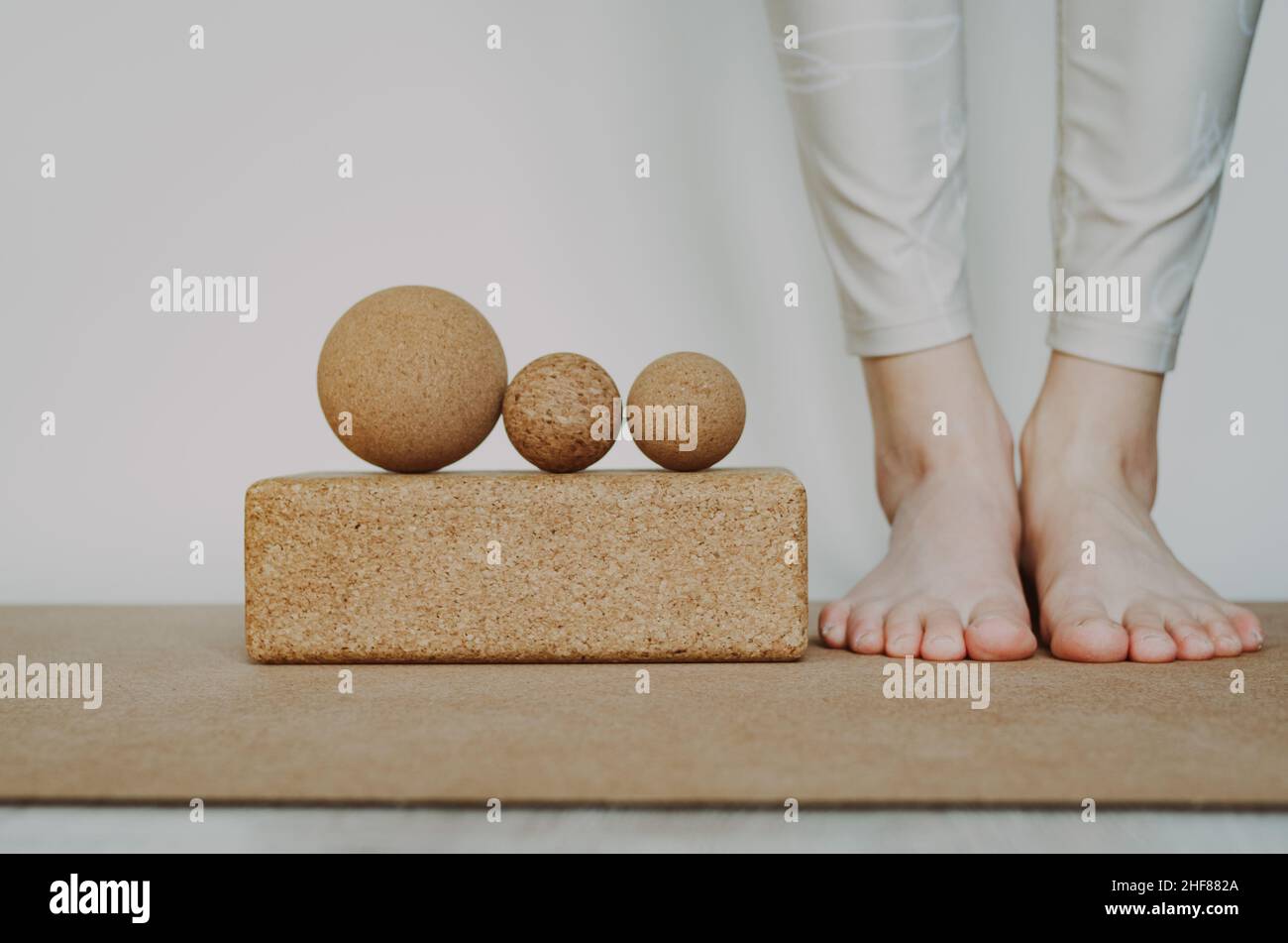 Les pieds de la personne se tenant près de trois balles de massage en liège pour la structure d'affichage sur un bloc de liège sur un tapis de yoga en liège. Concept : accessoires écologiques et biodégradables Banque D'Images