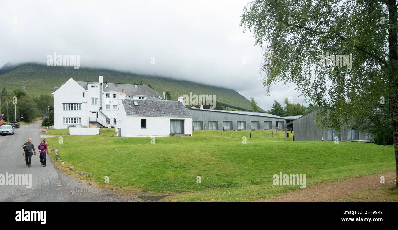 Deux randonneurs marchent derrière l'arrière de l'hôtel Bridge of Orchy, un 1930s mis à jour, tandis que les nuages descendent sur la colline en arrière-plan. Banque D'Images