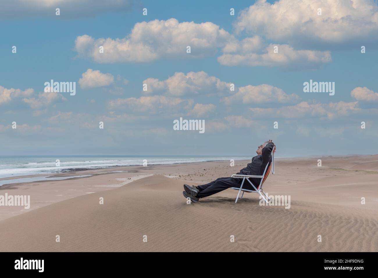 Homme adulte couché sur une chaise longue de plage en face de la mer Banque D'Images