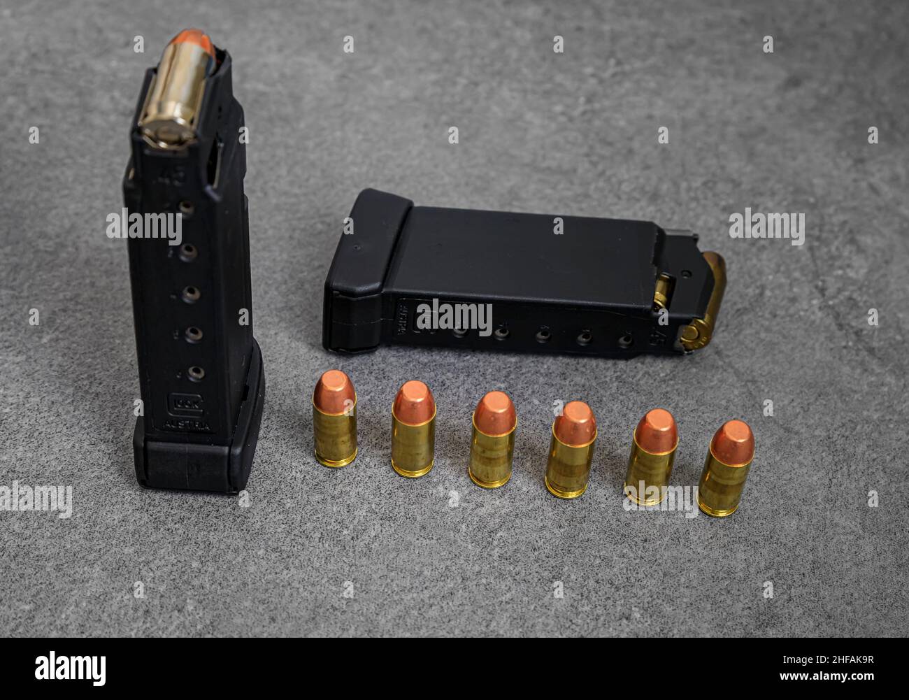 45 balles creuses et blouson plein métal de calibre ACP chargées dans des magasins de pistolet à main et des ronds non tirés alignés sur une surface en pierre Banque D'Images