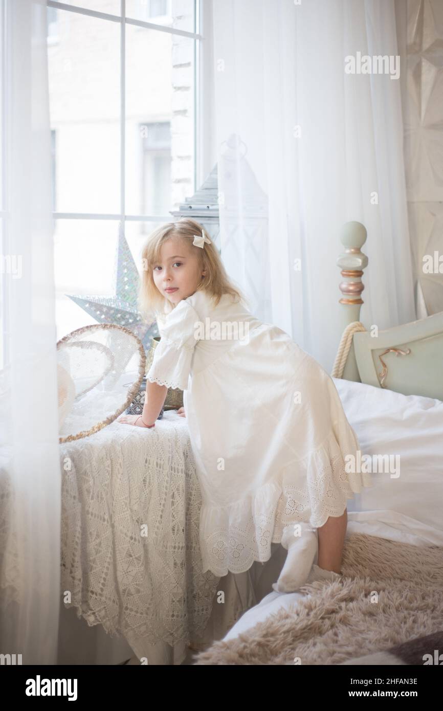 Petite fille mignonne près de la fenêtre dans sa chambre. Vacances d'hiver, style vintage. Banque D'Images