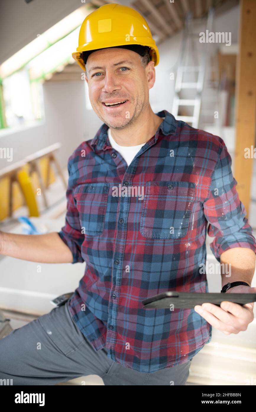 homme d'âge moyen sur le chantier avec un casque jaune et une chemise à carreaux travaillant avec sa tablette Banque D'Images