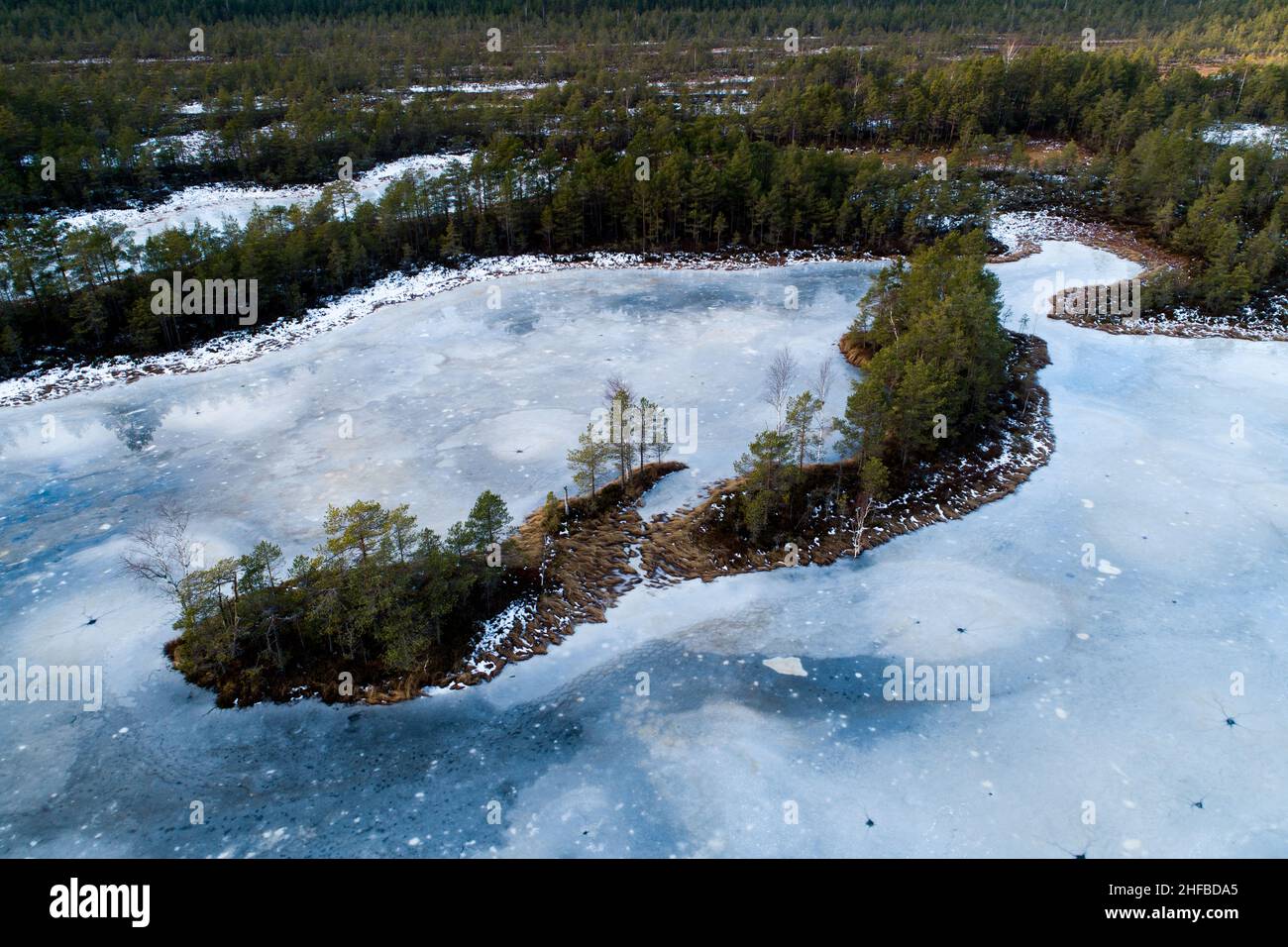 Une vue aérienne stupéfiante sur un lac de tourbière gelé avec une petite île dans la nature estonienne. Banque D'Images
