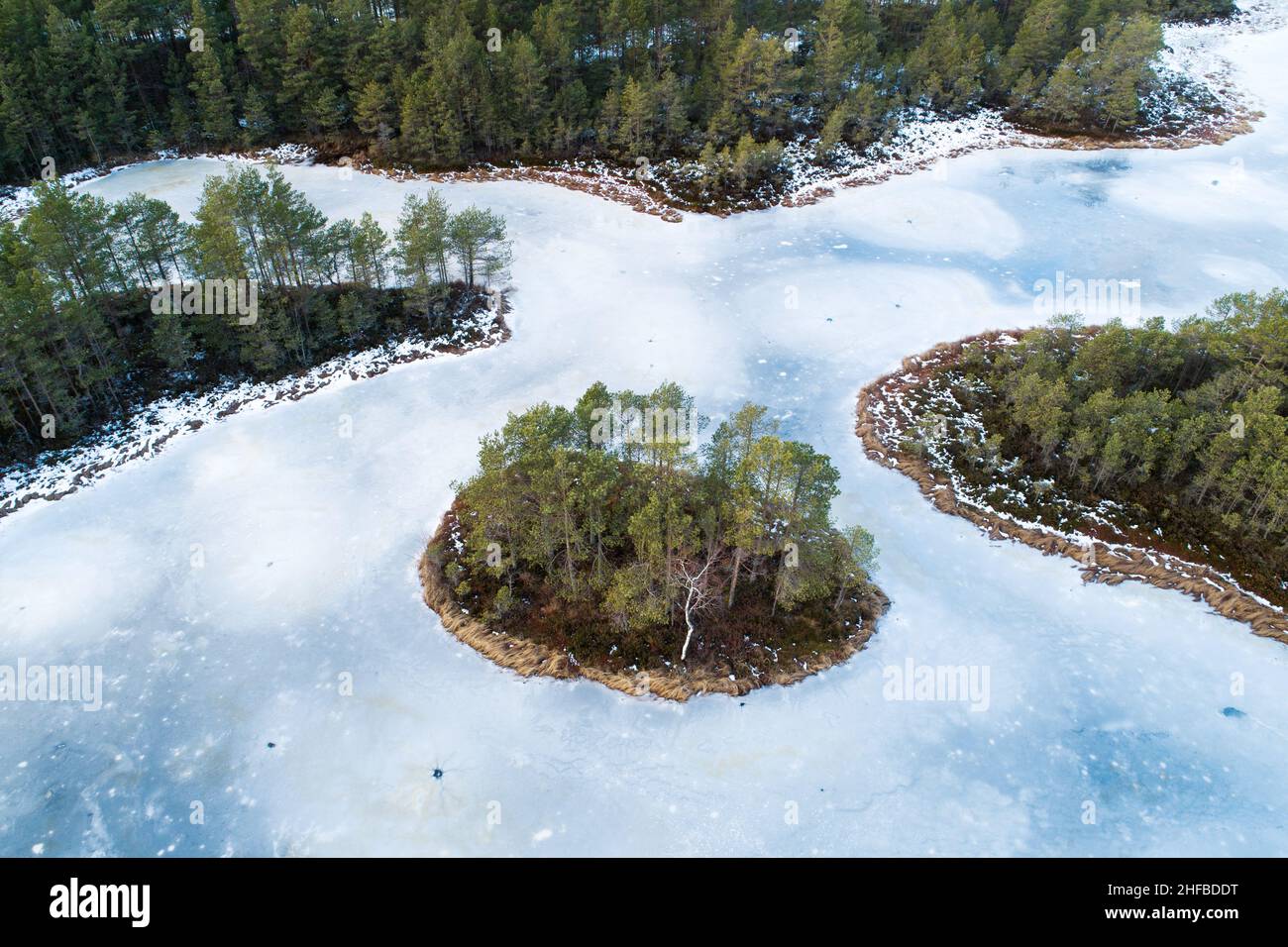 Une vue aérienne stupéfiante sur un lac de tourbière gelé avec une petite île dans la nature estonienne. Banque D'Images