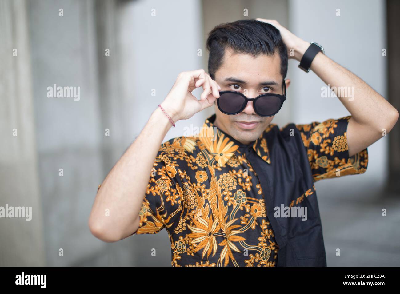 Un jeune mannequin vêtu de Batik indonésien porte et tient des lunettes de soleil sur fond de bokeh au long Museum, West Bund, Shanghai, Chine Banque D'Images