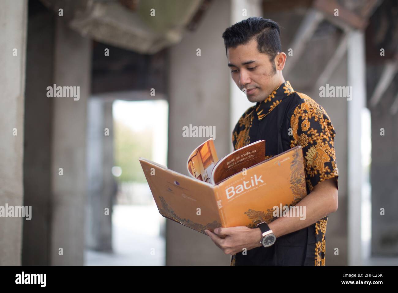 Un jeune modèle masculin habillé en indonésien Batik est en train de lire un livre intitulé Batik au long Museum, West Bund, Shanghai Chine Banque D'Images