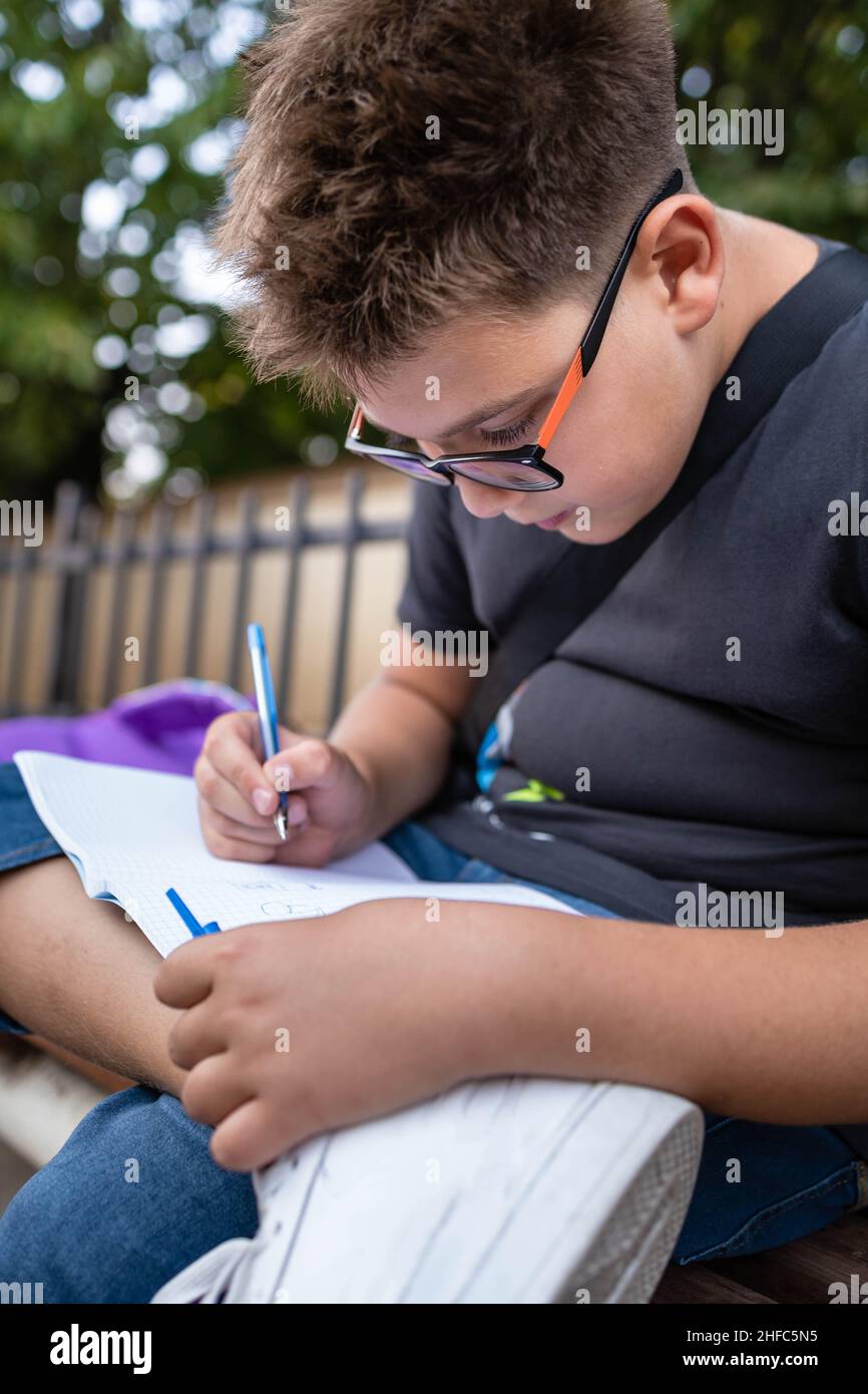 Petit garçon d'école avec des lunettes écrivant les devoirs à l'extérieur Banque D'Images