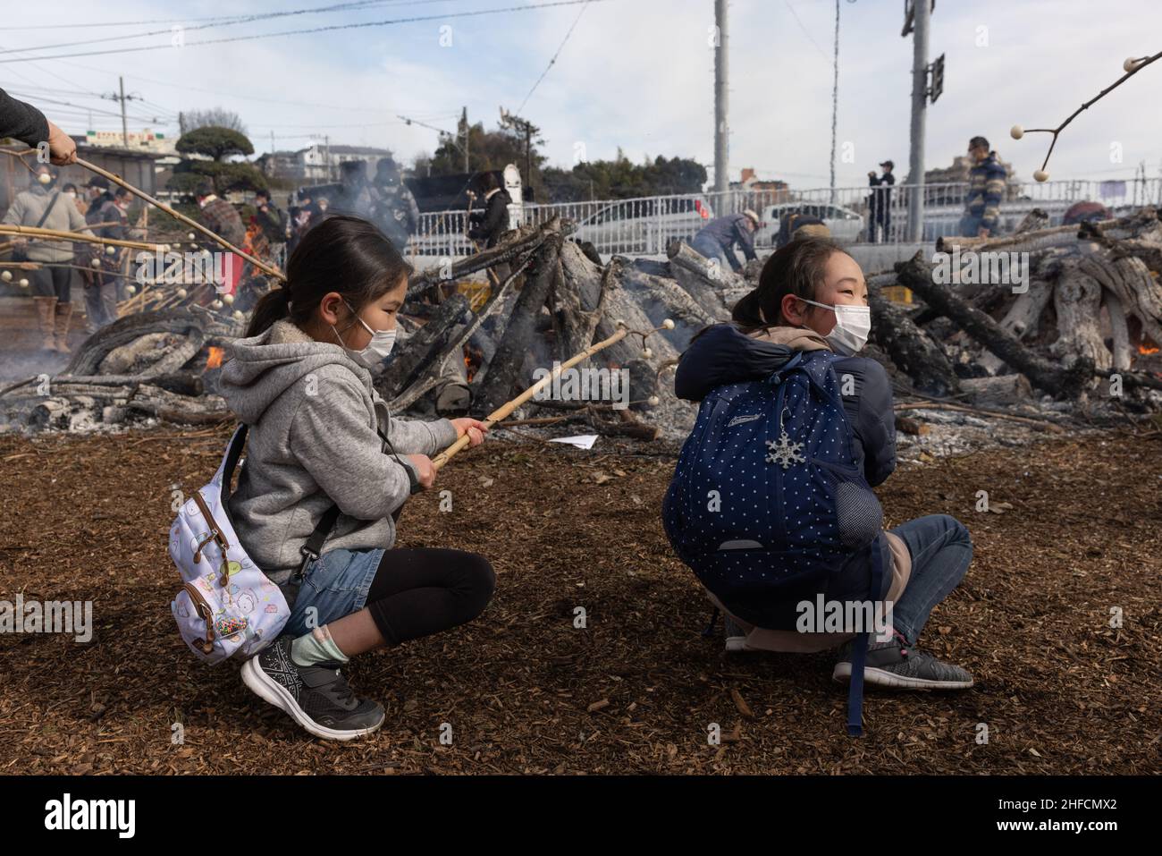Les filles avec des masques rôties Dango (gâteau de riz Mochi) pendant Dondo-Yaki à Aobadai.Dondo-Yaki est un événement traditionnel qui se tient habituellement à la mi-janvier et est considéré comme la fin de la fête du nouvel an au Japon.Au cours de cet événement Shimekazari (porte-bonheur) qui ont été utilisés pour attirer les dieux aux maisons des gens sont brûlés dans une cérémonie Shinto appelée Oharai.Il est exécuté pour garder la malchance loin des gens.Après l'arrêt du feu, le Dango (gâteau de riz mochi) ou les patates douces sont rôties au-dessus du feu de camp.L'origine de Dondo-Yaki remonte à la période Heian où les nobles brûlaient du bambou dans le thei Banque D'Images