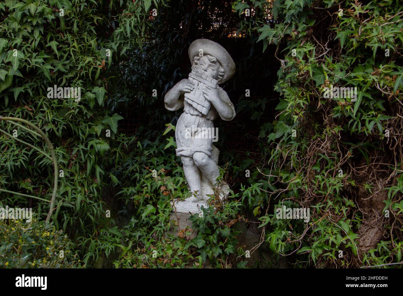 Ancienne statue blanche d'un garçon jouant une poêle flûte entourée d'ivy Banque D'Images