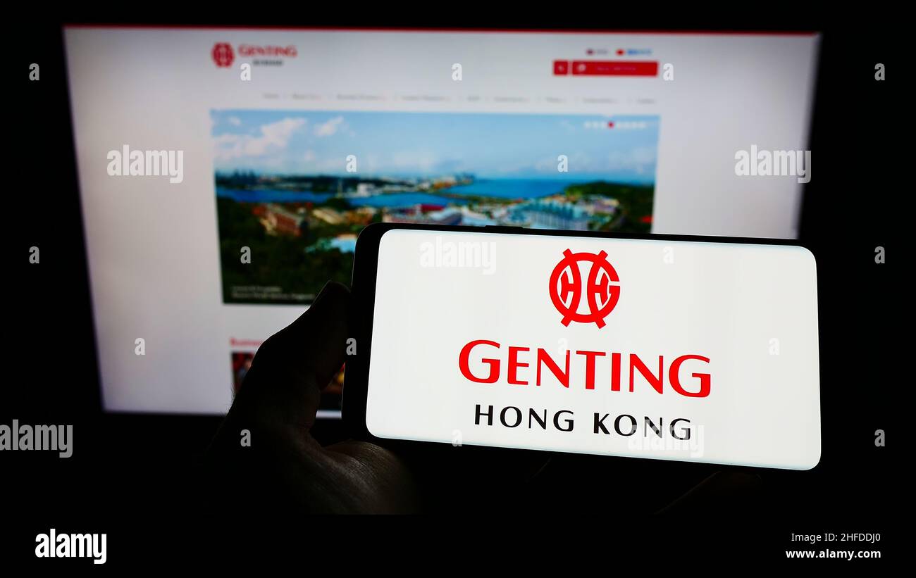 Personne tenant un téléphone portable avec le logo de la société de tourisme Genting Hong Kong Limited à l'écran en face de la page Web d'affaires.Mise au point sur l'affichage du téléphone. Banque D'Images