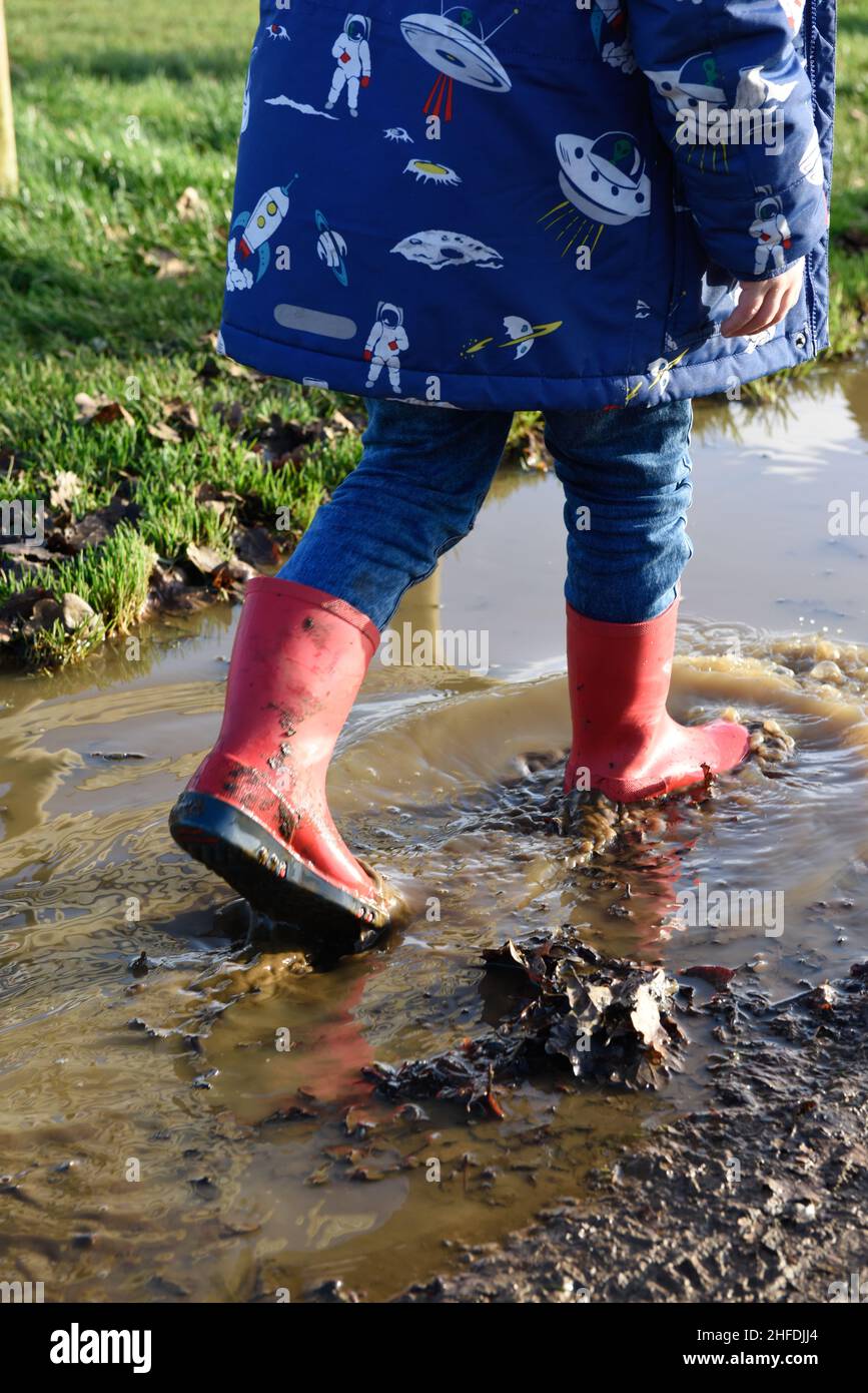 Garçon dans des bottes rouges éclaboussant dans des flaques d'eau Banque D'Images