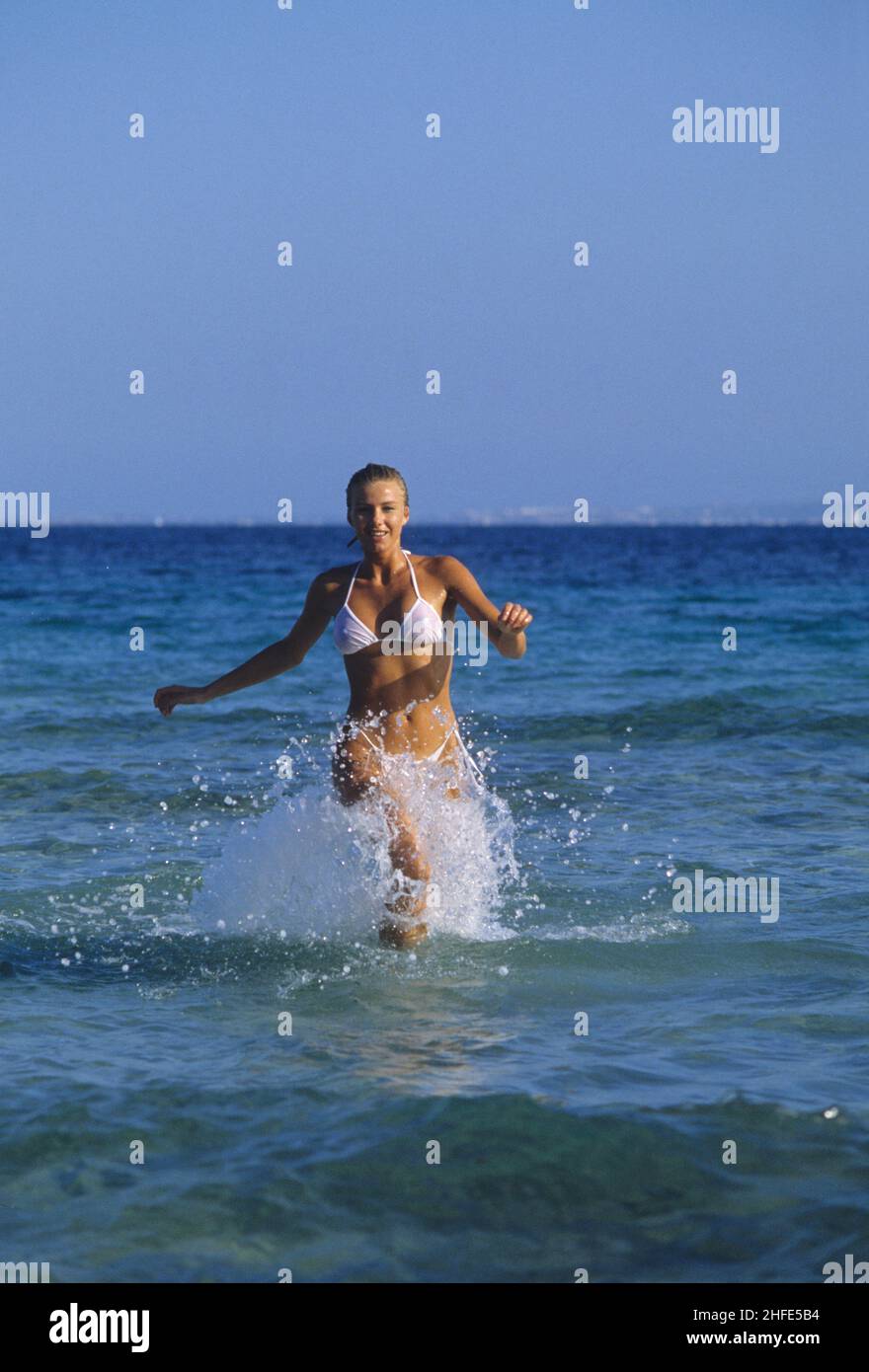 cheveux blond attrayant sportive beauté courant devant bleu éclaboussant ciel eau de mer fond Banque D'Images