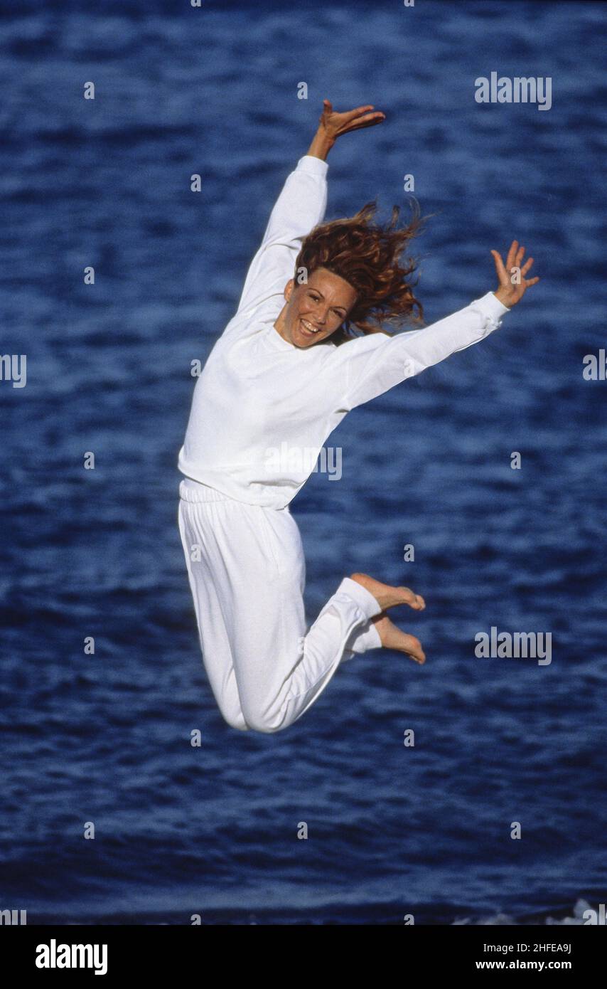 Cheveux bruns silhouette de femme attrayante sur la plage bras vers le haut caméra avant eau de mer arrière-plan saut gymnatique Banque D'Images