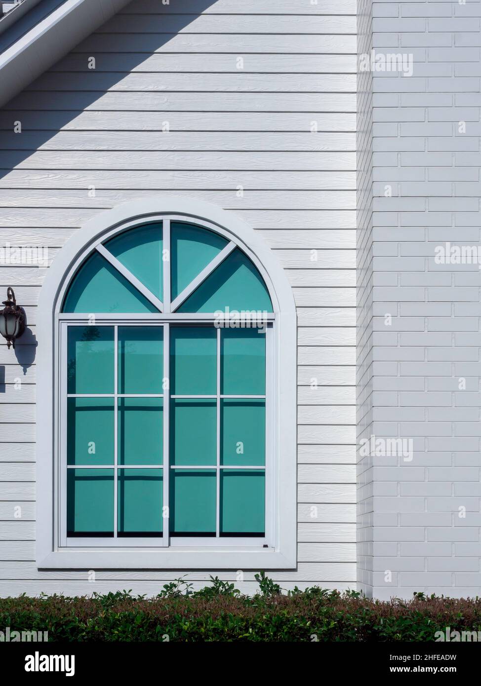 Une maison blanche avec fenêtre en verre, cadre incurvé, rideau vert sur le grand résident en bois blanc, style vertical, vue de l'extérieur. Banque D'Images