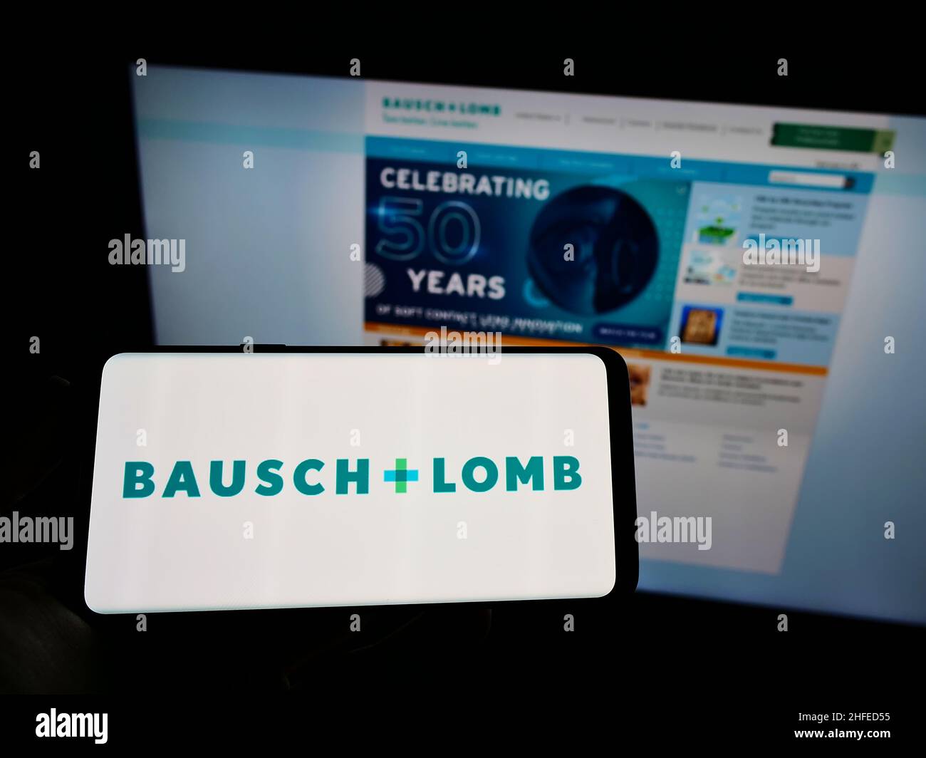 Personne tenant un smartphone avec le logo de la société canadienne de santé oculaire Bausch + Lomb à l'écran devant le site Web.Mise au point sur l'affichage du téléphone. Banque D'Images