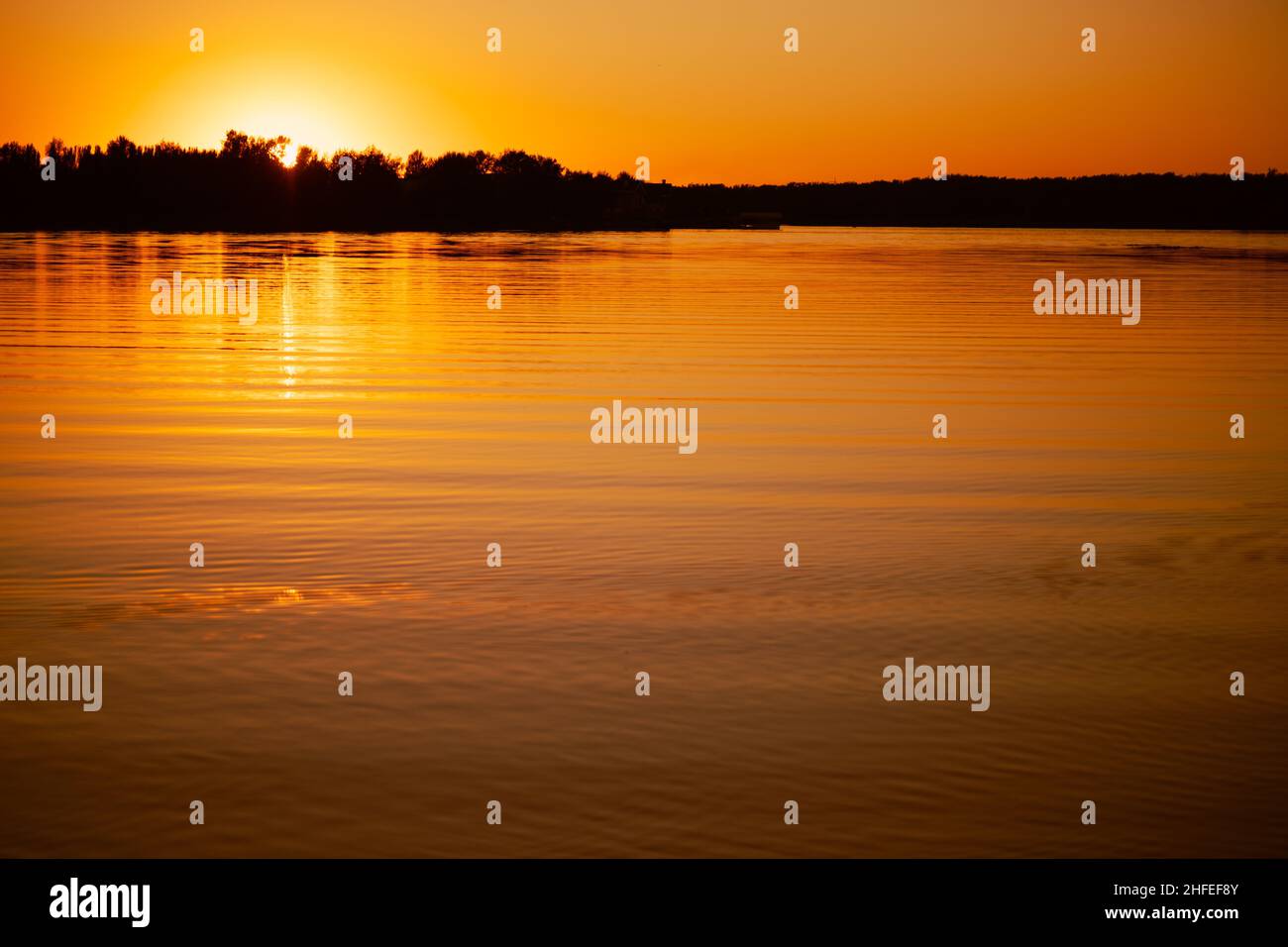 Lac brillant avec le soleil se coucher sous l'horizon et couvrant avec des rayons de surface de l'eau avec des arbres sombres en arrière-plan.Vue étonnante pleine de jaune et Banque D'Images