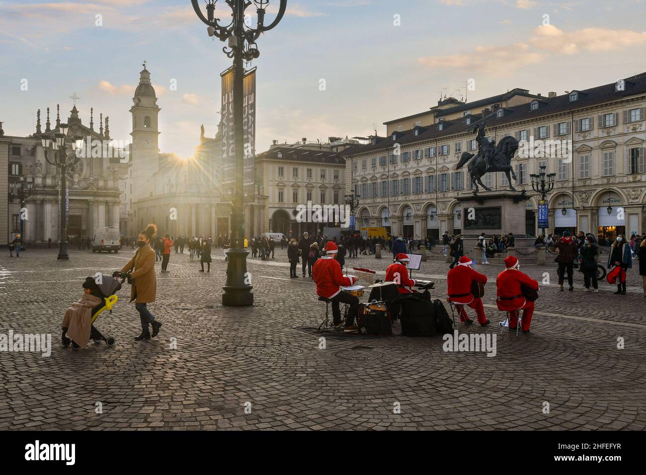 Vue en contre-jour d'un petit groupe habillé comme le Père Noël et jouant des chansons de Noël sur la Piazza San Carlo au coucher du soleil, Turin, Piémont, Italie Banque D'Images