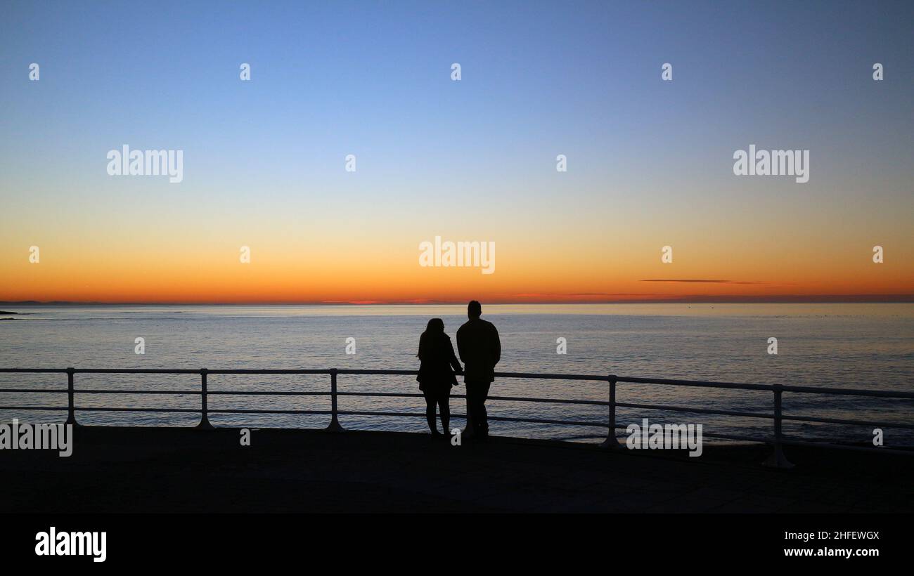Aberystwyth, pays de Galles, Royaume-Uni - 14-Jan-2022 - deux personnes regardent la lueur du coucher de soleil à Aberystwyth, pays de Galles, Royaume-Uni, alors qu'une période de haute pression apporte un climat calme et stable au Royaume-Uni - photo Credit: John Gilbey Banque D'Images