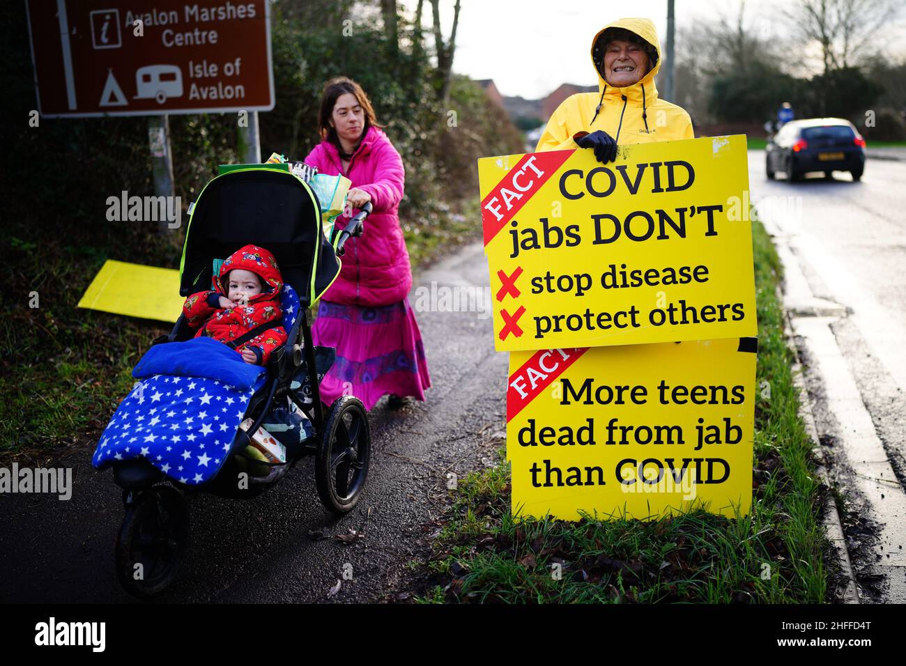 Une femme pousse un enfant devant une personne tenant des panneaux anti-vax sur le côté de la voie de transport de A39 à Glastonbury, dans le Somerset.Date de la photo: Dimanche 16 janvier 2022. Banque D'Images
