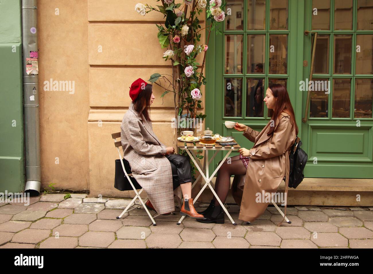 Lviv, Ukraine - 26.09.2021: Deux jeunes femmes boivent du thé ou du café à l'extérieur dans le contexte de la vieille ville.Personnes, communication et amitié concept: Femmes Banque D'Images