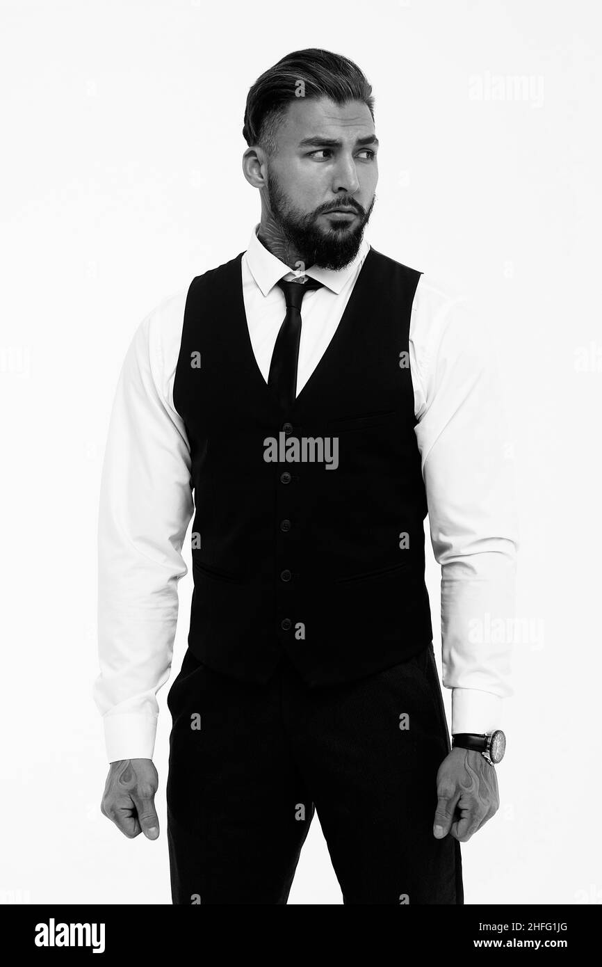 Homme hispanique barbu dans un gilet sombre et une chemise blanche avec  cravate regardant l'appareil photo avec les mains dans les poches en studio  Photo Stock - Alamy