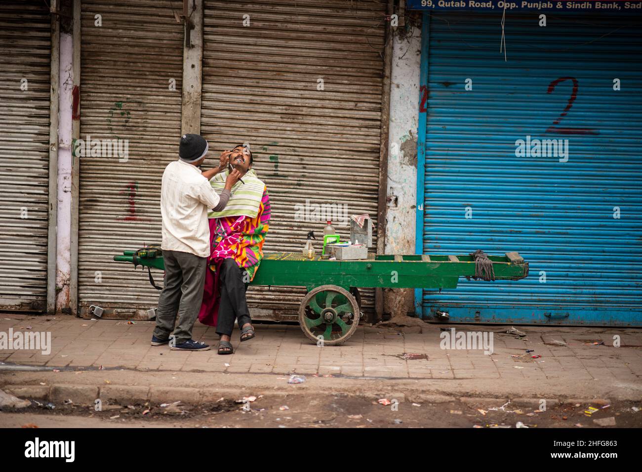 New Delhi, Inde.16th janvier 2022.Un barbier local a vu raser un travailleur migrant assis sur une voiturette garée devant les boutiques fermées de Sadar Bazar.en raison de la montée des affaires Covid-19 à Delhi, le gouvernement a imposé le couvre-feu du week-end.Le ministre de la Santé de Delhi, Satyendar Jain, a déclaré que le couvre-feu du week-end et les restrictions préventives contribuaient à freiner la propagation de Covid-19 dans la capitale nationale.Delhi a signalé 20 718 cas de covid et 30 décès le 16th janvier 2022, alors que le taux de positivité était de 30,64 %.Crédit : SOPA Images Limited/Alamy Live News Banque D'Images