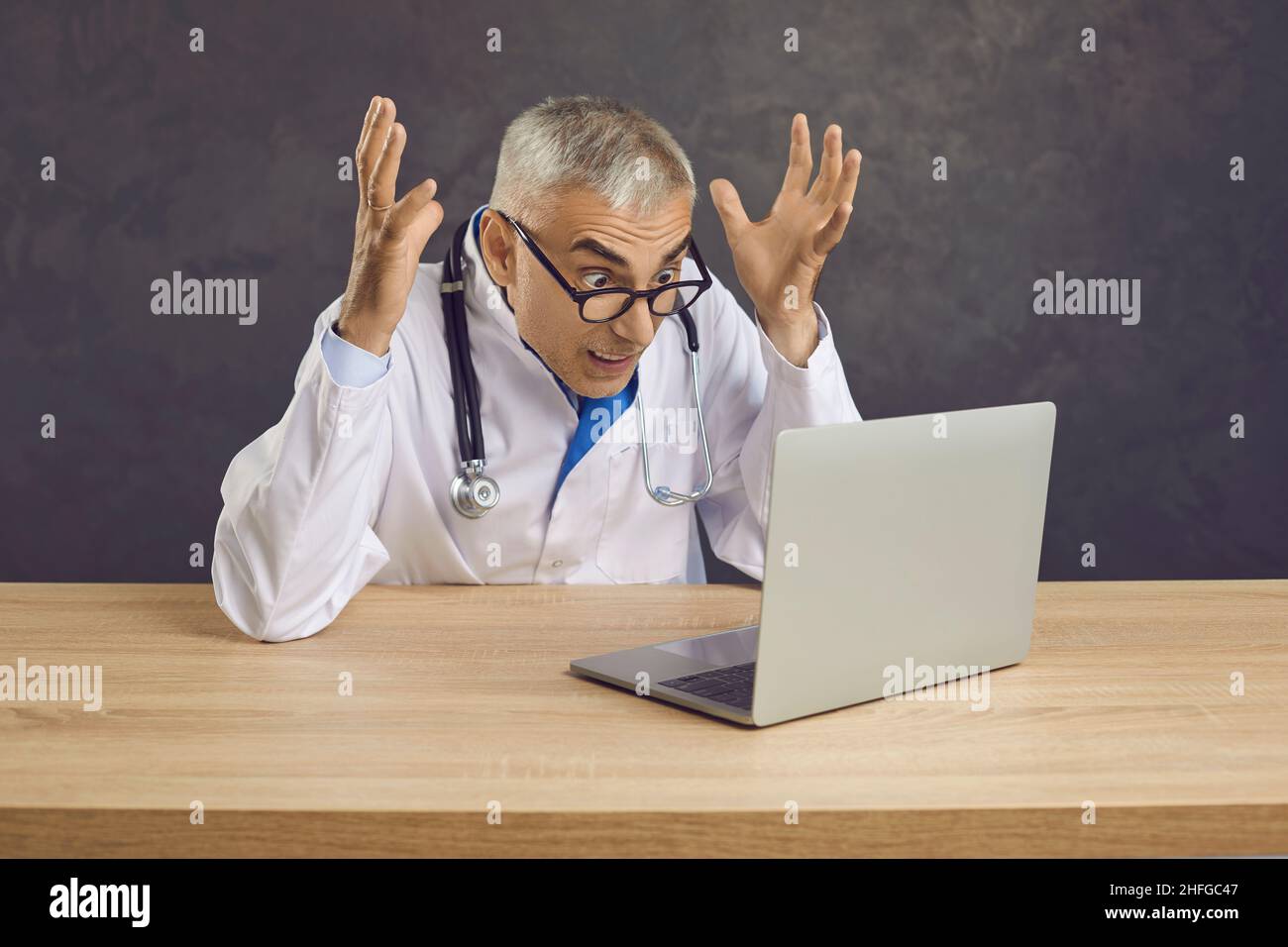 Un médecin senior fou et en colère criait à la frustration en regardant l'écran d'un ordinateur portable. Banque D'Images