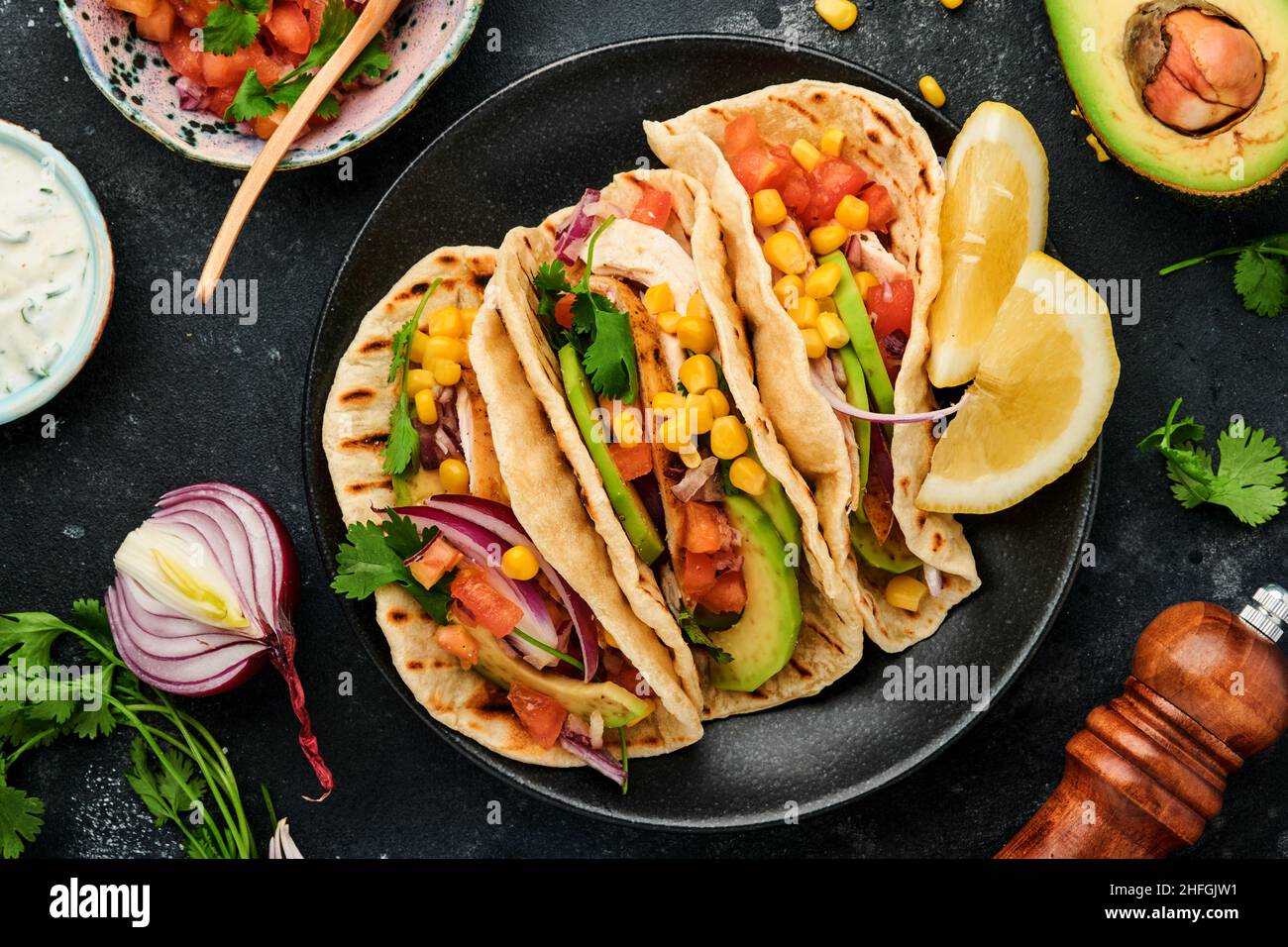 Tacos mexicains avec poulet grillé, avocat, grains de maïs, tomate, oignon, coriandre et salsa à la table en pierre noire. Cuisine mexicaine traditionnelle et latino-américaine Banque D'Images