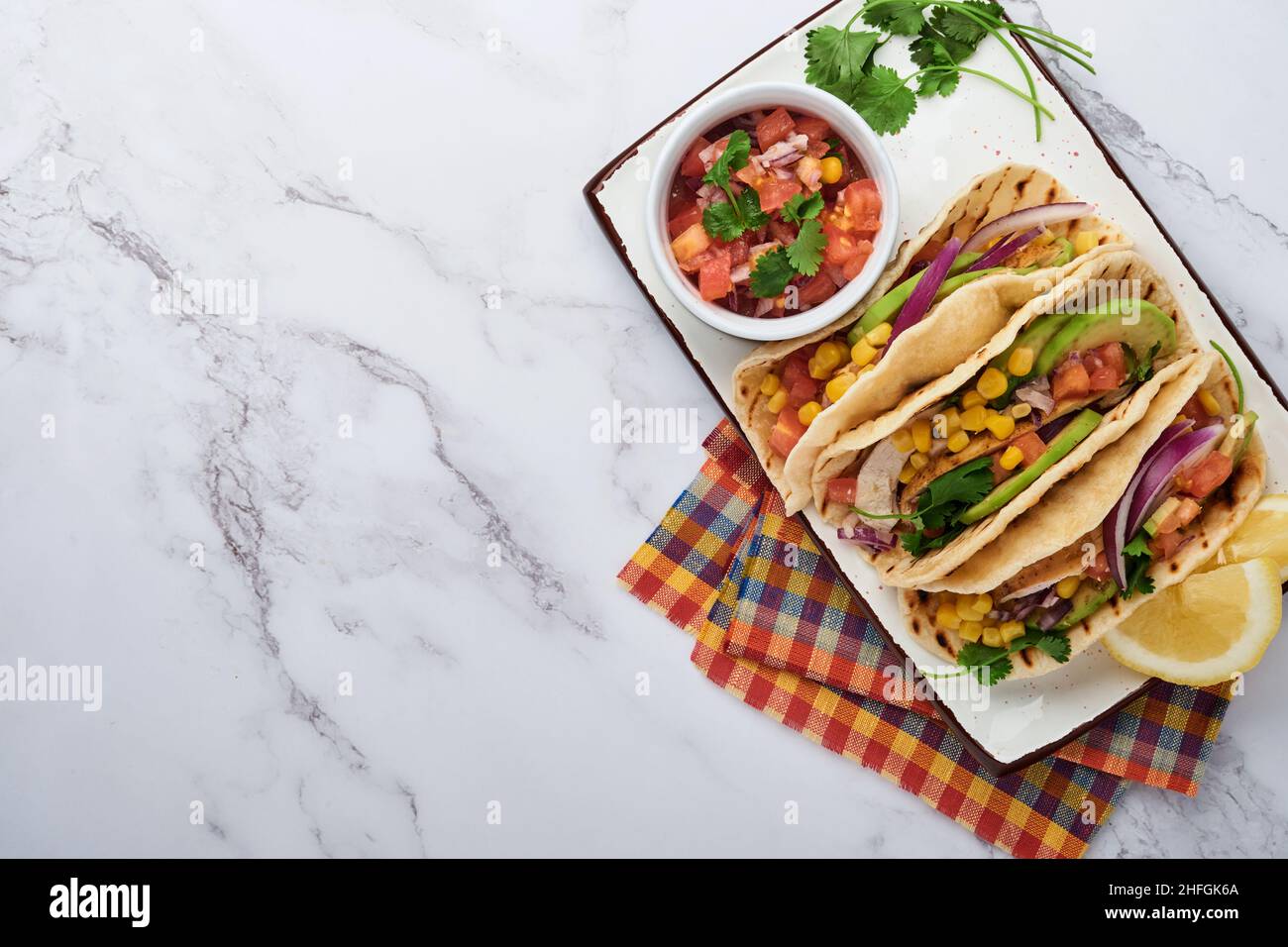 Tacos mexicains avec poulet grillé, avocat, grains de maïs, tomate, oignon, coriandre et salsa à la table en pierre blanche. Cuisine mexicaine traditionnelle et latino-américaine Banque D'Images