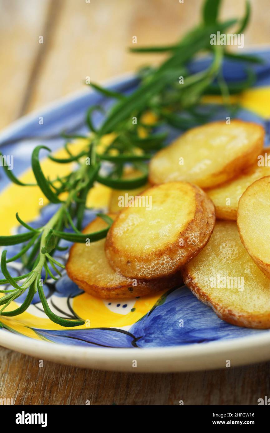 Tranches de pommes de terre frites et romarin frais sur assiette vintage Banque D'Images