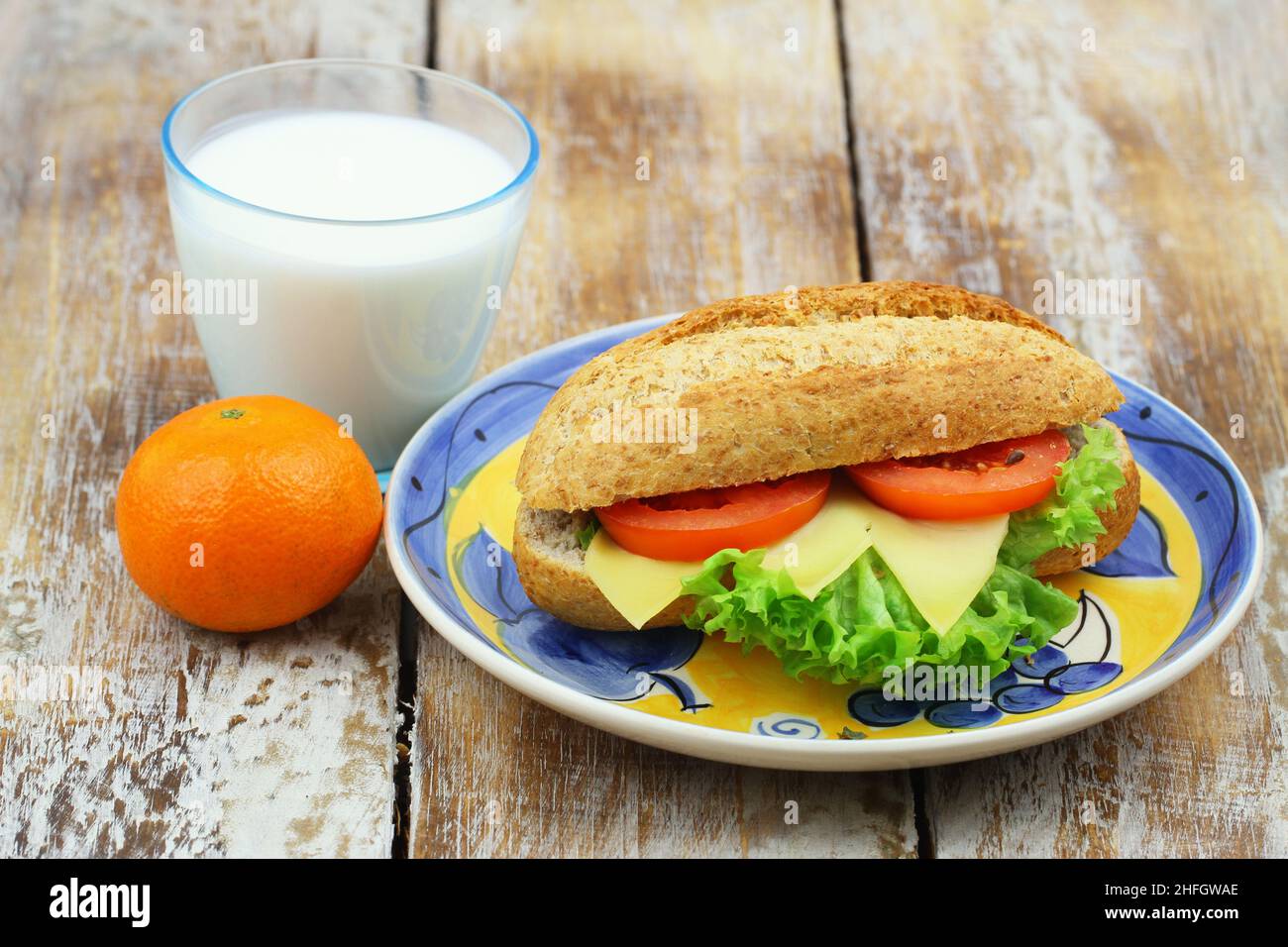 Petit déjeuner ou déjeuner sain : sandwich au fromage brun avec laitue et tomate, mandarine et verre de lait frais Banque D'Images