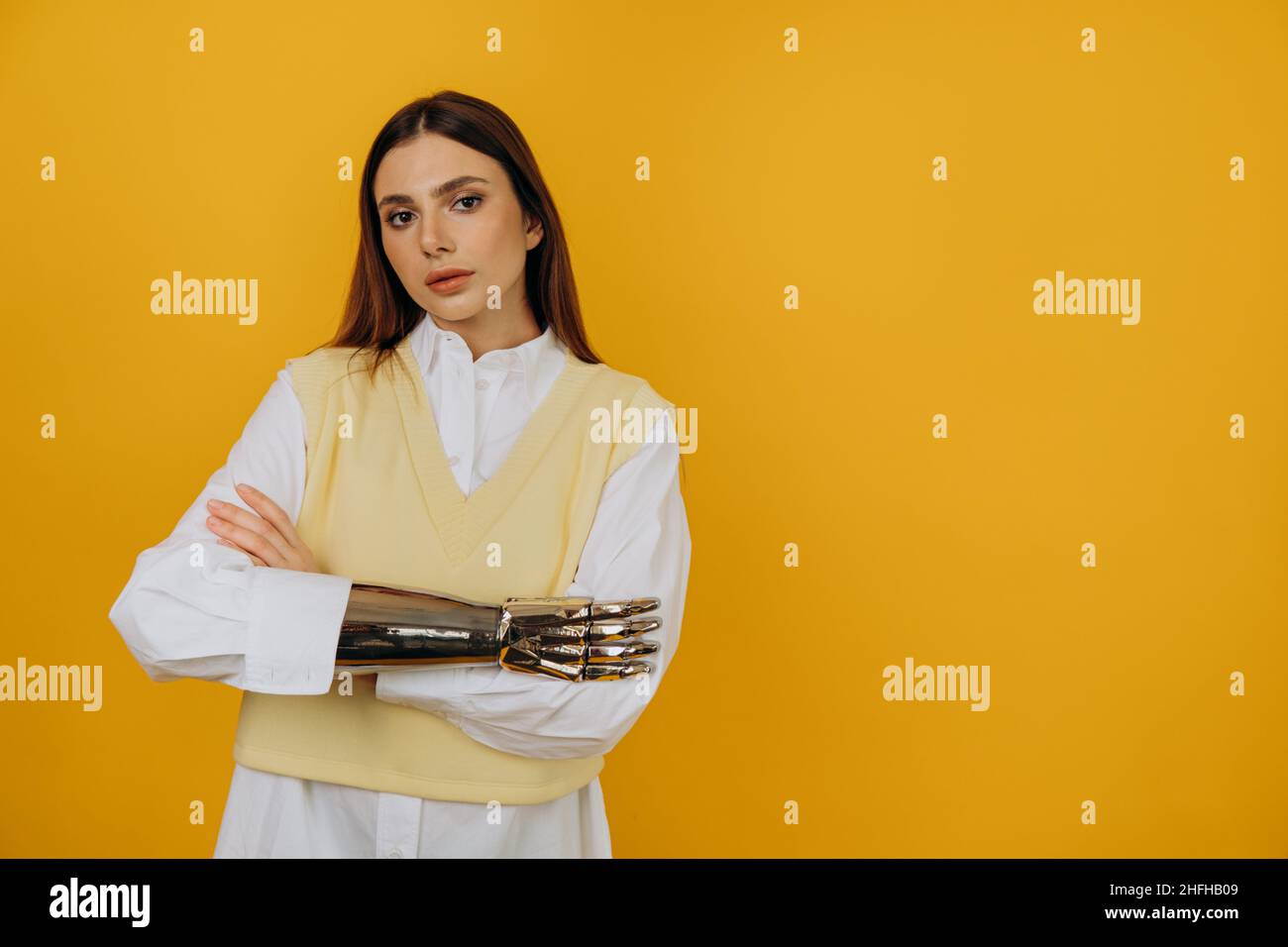 Jeune femme confiante en chemise et gilet avec nouvelle prothèse bionique croise les bras debout sur fond jaune vue rapprochée Banque D'Images