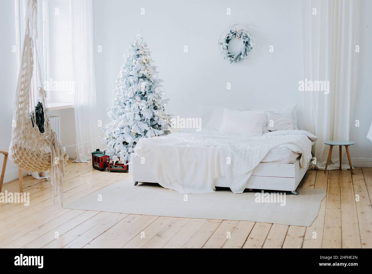 Cette chambre lumineuse et spacieuse dispose d''un grand lit avec des draps blancs, d''un élégant sapin de Noël lumineux et d''une couronne au mur.Intérieur mignon et festif. Banque D'Images