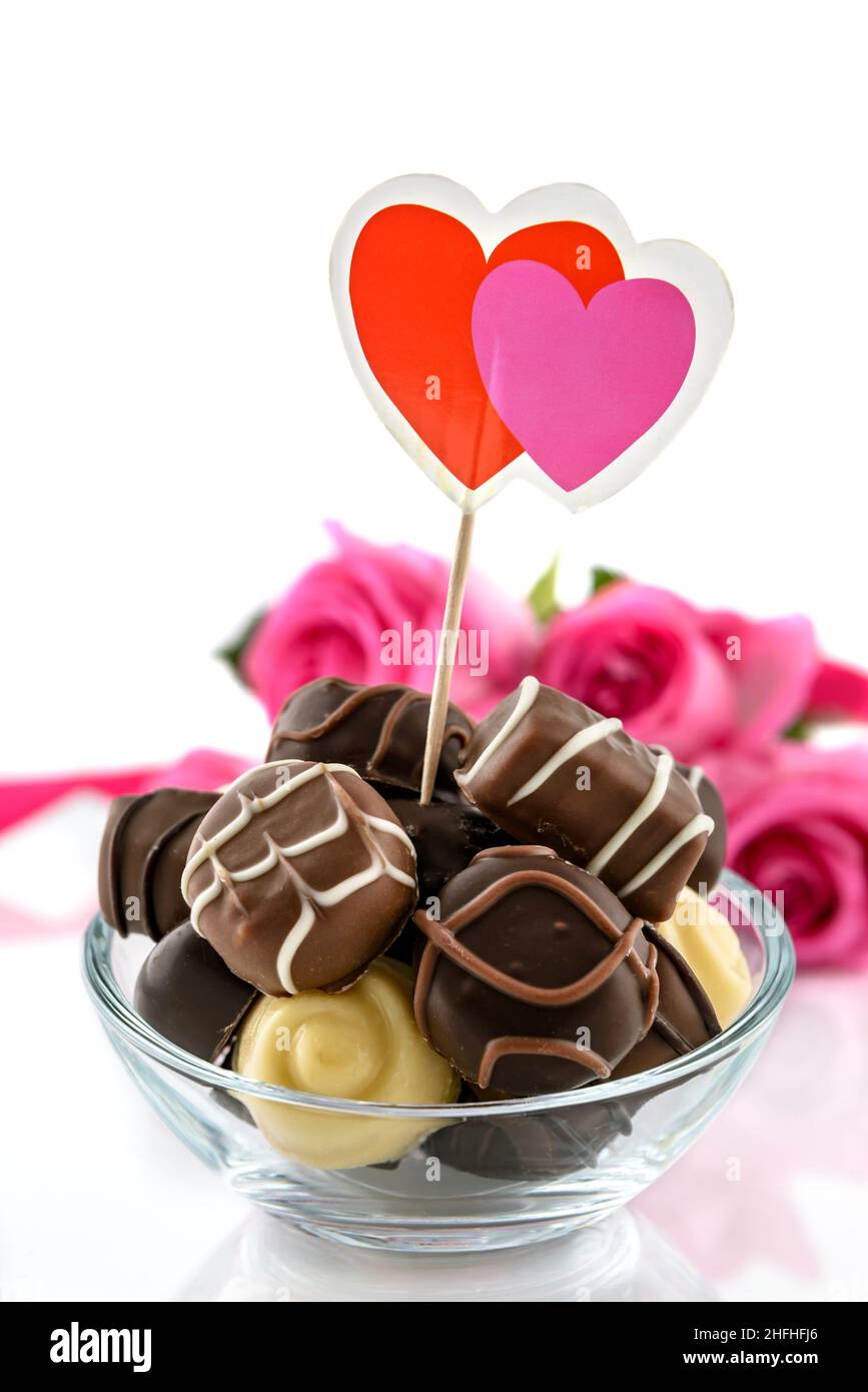 Pralines au chocolat dans un bol en verre et bouquet de roses roses sur fond blanc.Concept de la Saint-Valentin et de la fête des femmes, mise au point sélective. Banque D'Images