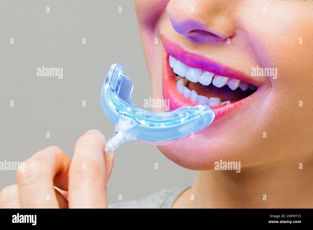 Une jeune femme est engagée dans le blanchiment des dents à la maison. Complexe pour le blanchiment des dents avec lampe UV Banque D'Images